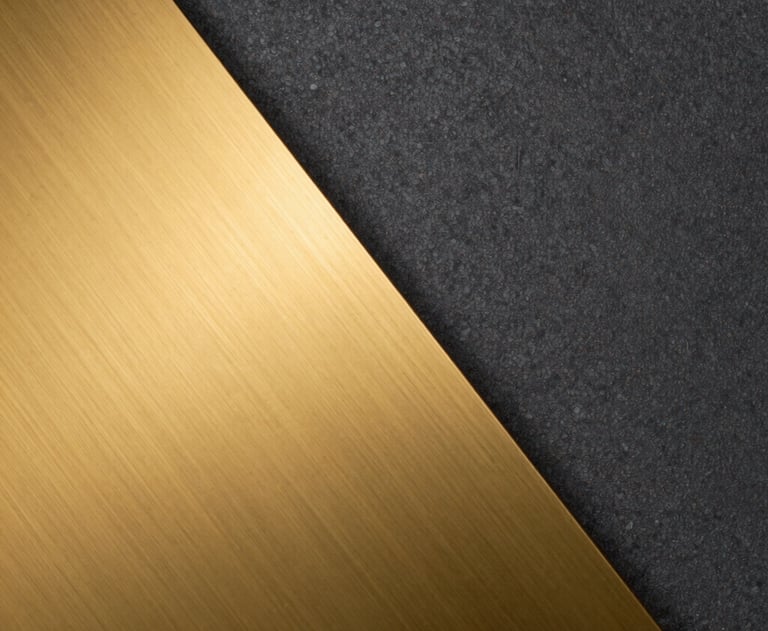 An abstract image showing the contrast between a smooth golden metal surface and a textured dark graphite wall, reflecting the brand colors.