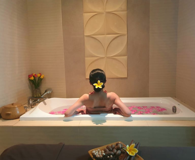 A woman relaxes in a luxury spa bathtub filled with pink flower petals for a wellness treatment.