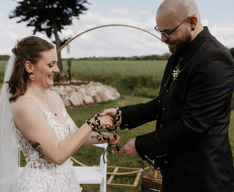 Knoten Ritual! das Hochzeitspaar bindet ein gold und schwarz geflechtetes Band um die eigenen Hände