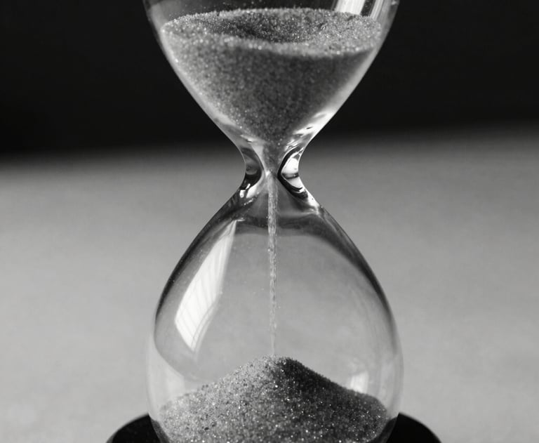 Close-up of an hourglass on a desk, the sand is flowing. High-contrast black and white style. Professional and philosophical. No people.
