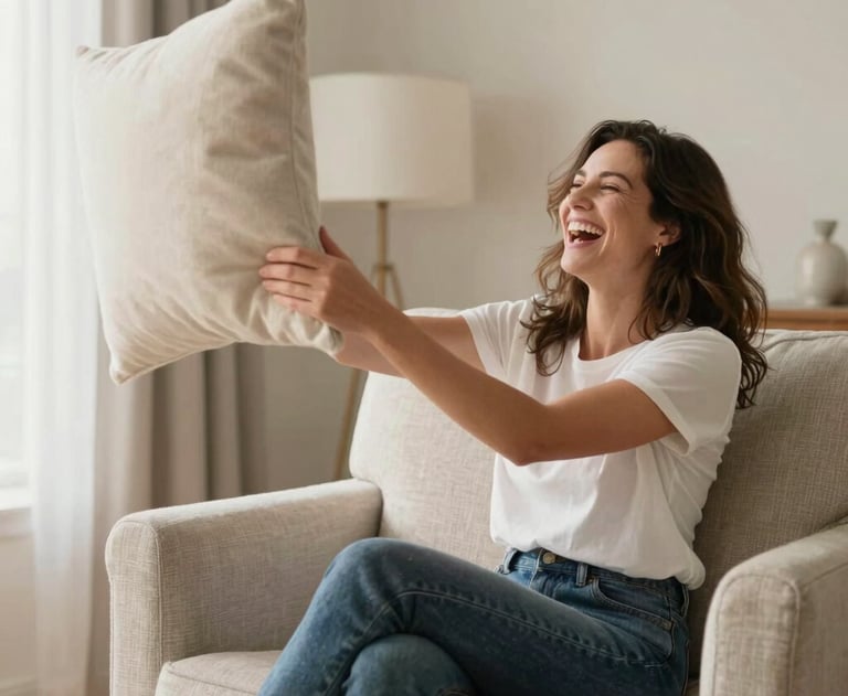 A warm, candid photo of a stylish mom laughing while sitting on a chic neutral armchair, playfully throwing a cream-colored throw pillow. Bright, funny, and beautiful atmosphere in a North American / US living room.