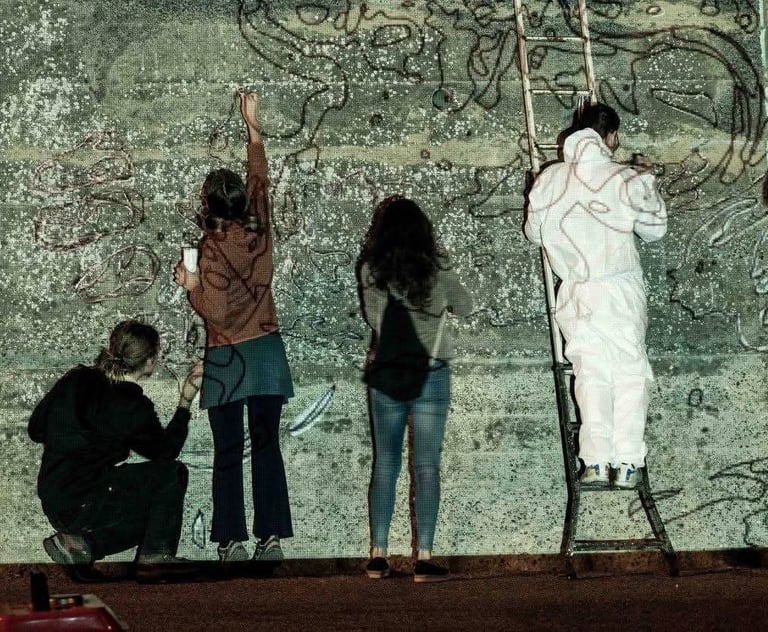 Group of people drawing on a projected wall, collective art workshop led by Poliops.