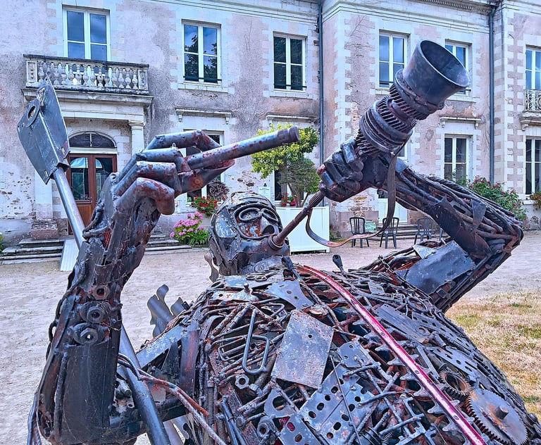 Intricate scrap metal sculpture of Capitaine Boyton outside a historic stone building in France.