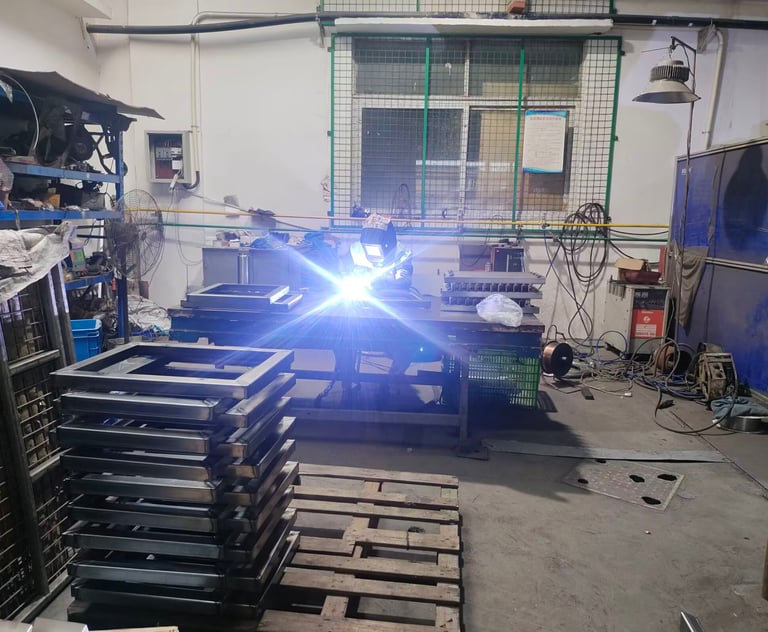 Professional welder in protective gear welding metal frames in an industrial workshop.