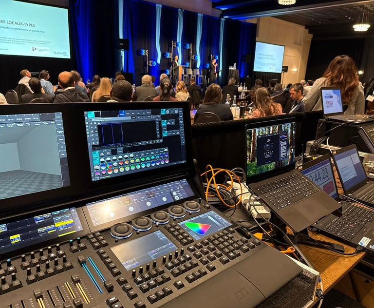 Professional lighting console and laptops at a live event production tech booth in a conference hall.
