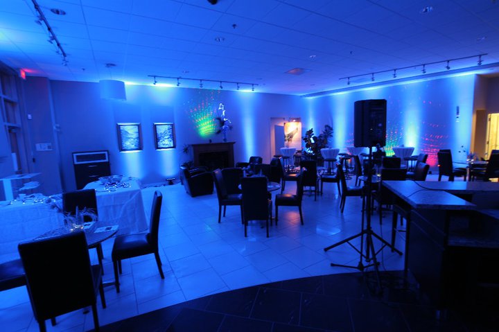 Modern event lounge with blue professional uplighting, cocktail tables, and black chairs.
