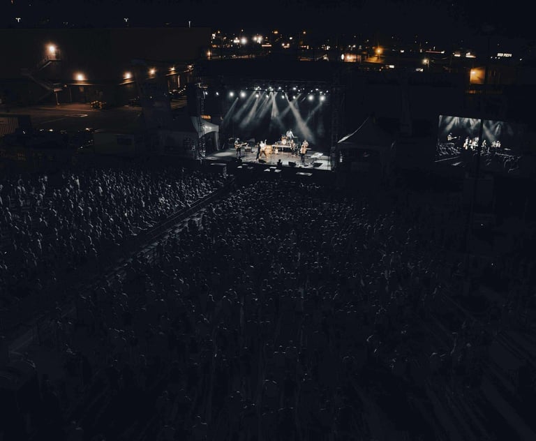 A band performs on a lit outdoor stage at night before a large crowd at a music festival.
