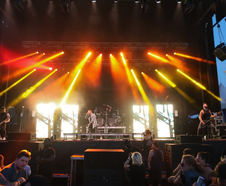 A rock band performs on a large outdoor stage with dramatic orange spotlights and stage lighting.