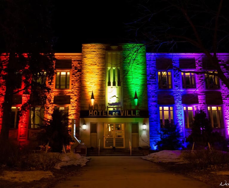 The Hotel de Ville building illuminated with vibrant rainbow pride colors at night.