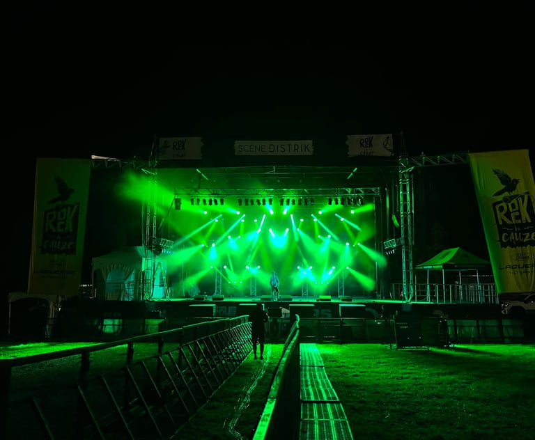 Live music stage at night with bright green spotlights and Rek la Cauze festival banners.