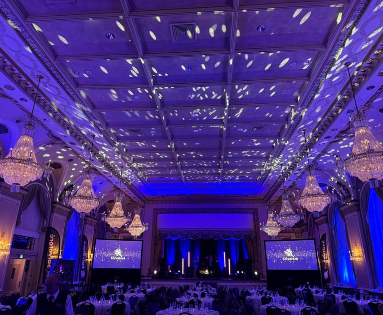 Elegant grand ballroom event space with crystal chandeliers and blue stage lighting for a corporate gala.