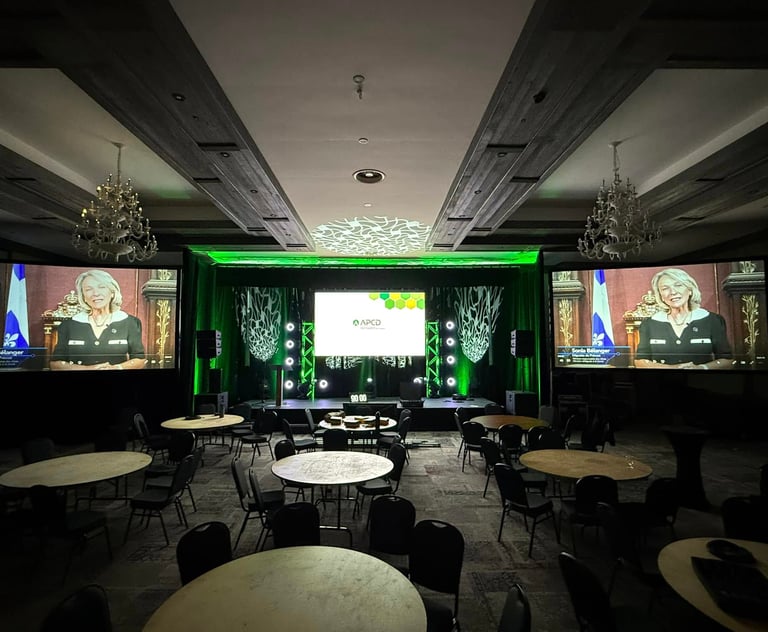 Professional ballroom conference setup with stage lighting, round banquet tables, and large projection screens.
