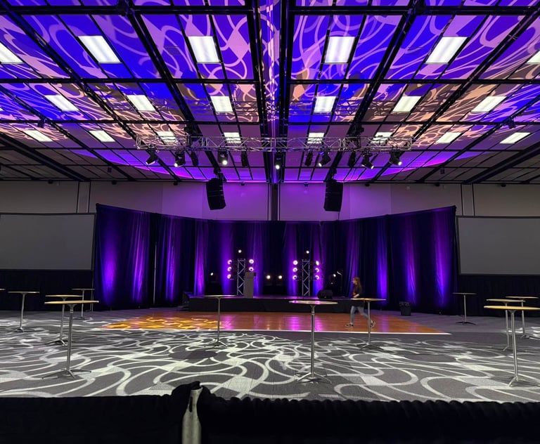 Grand ballroom event space with purple stage lighting, professional audiovisual setup, and high-top tables.