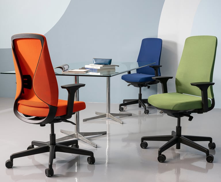 Three colorful Sensit T150 chairs in orange, blue, and green around a glass meeting table.