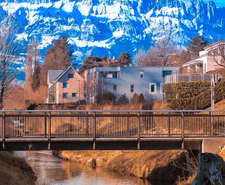 Scenic alpine town in Liechtenstein with modern homes, a small river and footbridge in the foregroun