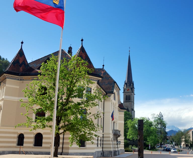 Vibrant spring scene of Vaduz, Liechtenstein, featuring the national flag waving in front of the his