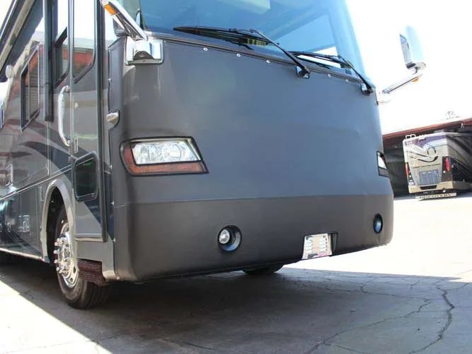 A motorhome with a black protective vinyl front mask cover parked on a paved lot.