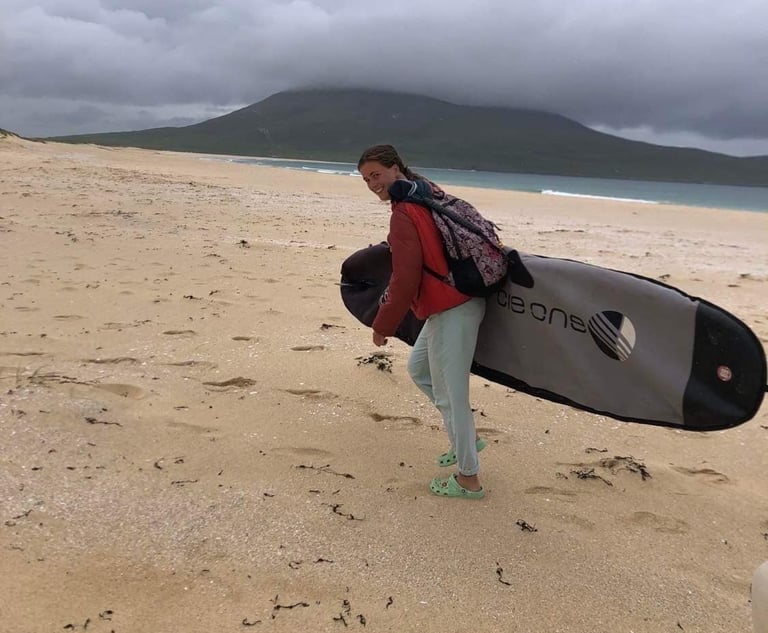 Stand up paddle board coach Erin walking along a snafy beach carrying a longboard.