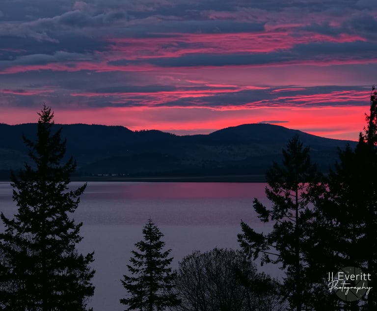 a sunrise sky with a pink sky and a mountain in the background overlooking a lake