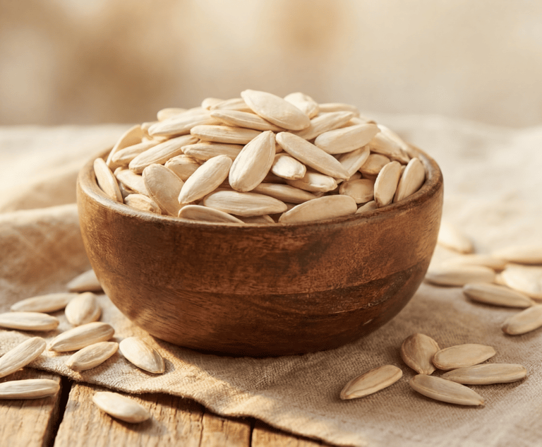 A rustic wooden bowl filled with roasted white pumpkin seeds on a burlap cloth.
