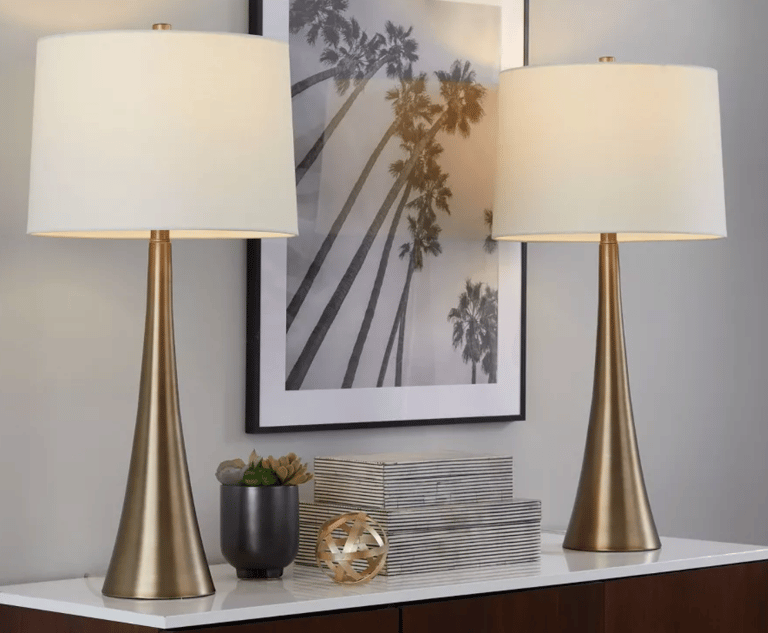 Pair of mid-century modern gold table lamps with white drum shades on a console table.