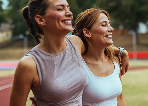 Two happy women in athletic wear smiling after a workout on an outdoor running track.