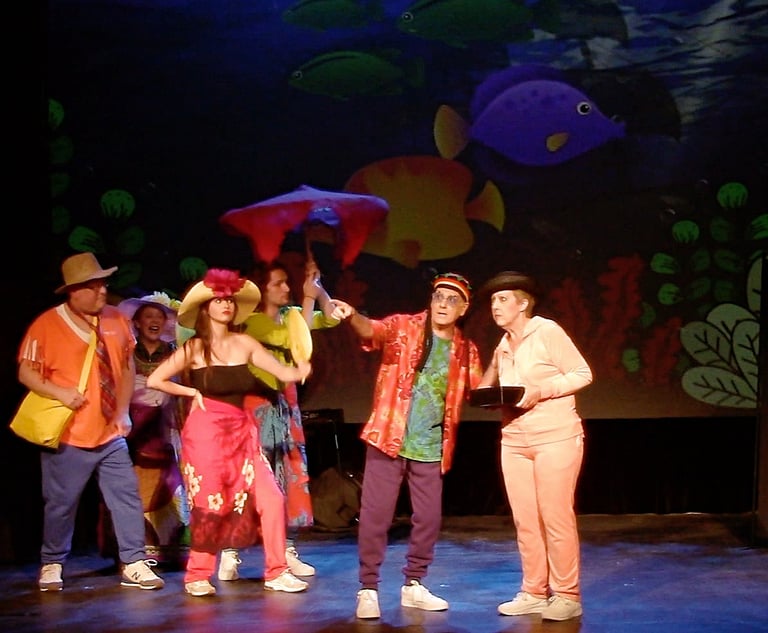 Actors in colorful costumes perform a comedy musical number with a tropical fish backdrop.