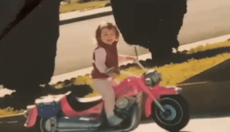 a little girl riding a pink motorcycle in a driveway
