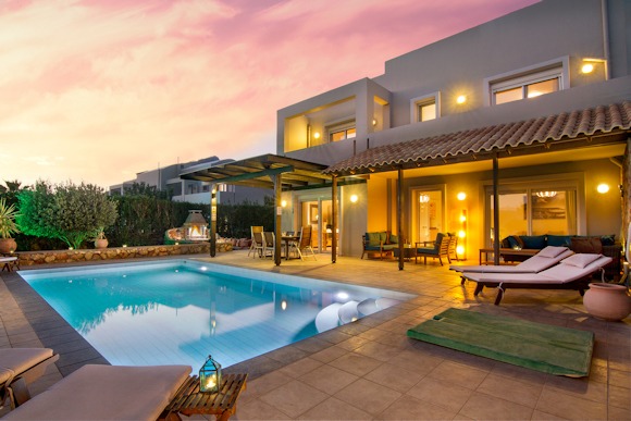 Luxury villa with private swimming pool and outdoor lounge area under a sunset sky.