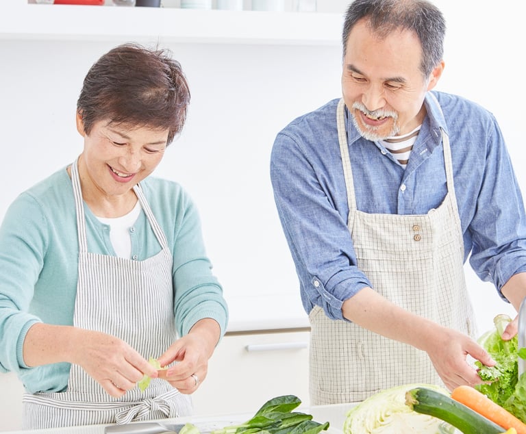 une femme et un homme souriant occupés a préparer un repas.