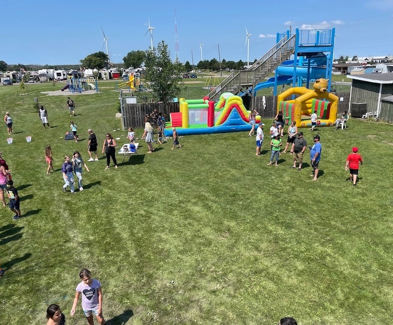 Families enjoy an outdoor summer festival at an RV park with inflatable bounce houses and a water slide.