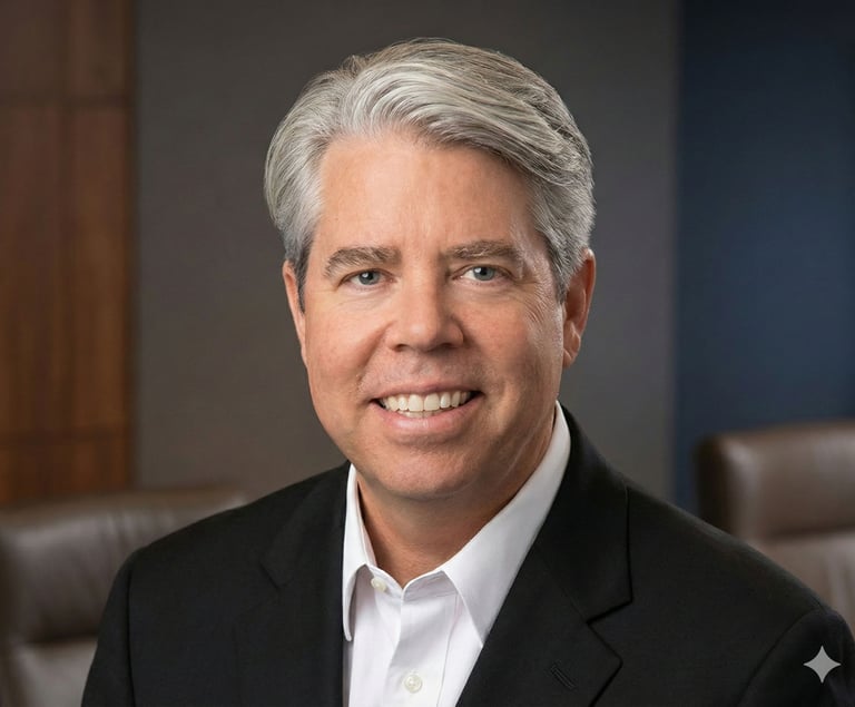 Professional headshot of a smiling male executive with grey hair in a black suit jacket and white shirt.