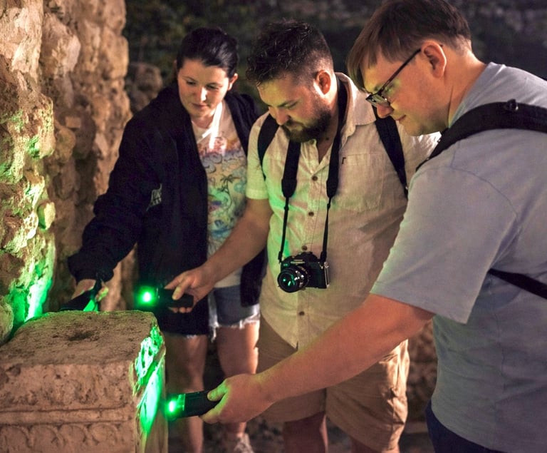 Tour participants examining ancient stone ruins with green UV lights during Athens Ghost Tour