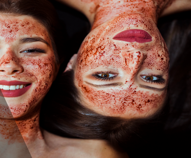 Two women with red face paint showcasing vampire facial treatment, a popular acne scar treatment in Vadodara