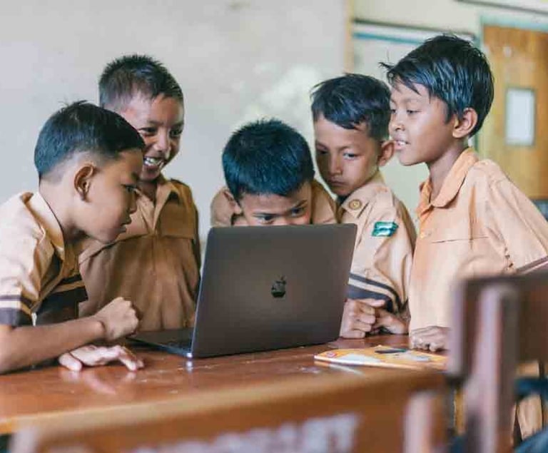 a group of children in school uniforms looking at a laptop