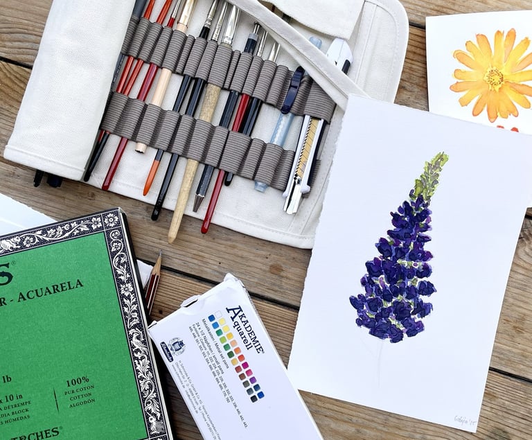 a bunch of art supplies: watercolour, pencil, brushes, paper on the table