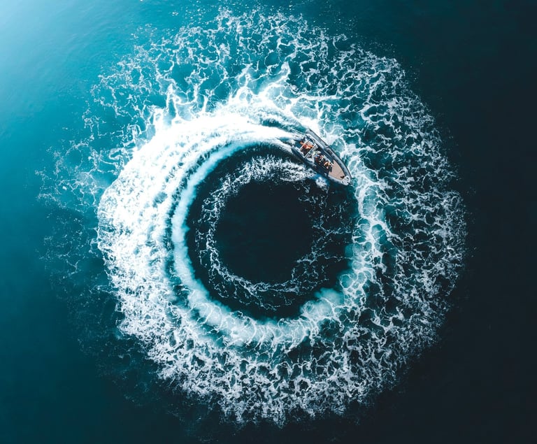 Aerial view of a motorboat creating a circular white foam wake in deep blue ocean water.