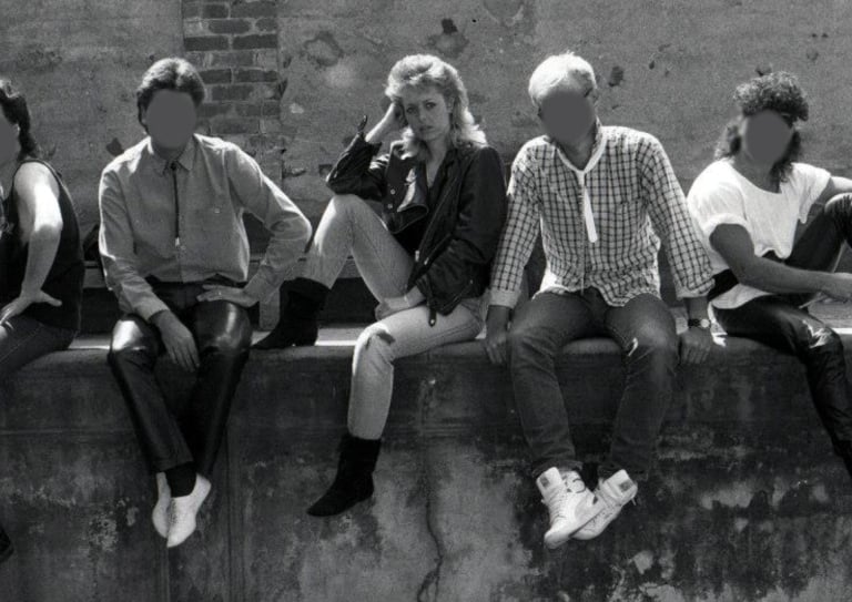 Black and white image of a young woman sitting on a wall with her four male band mates