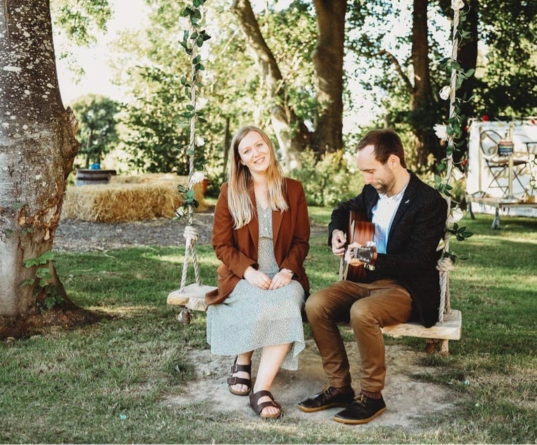 a man and woman sitting on a swing with a guitar at wedding