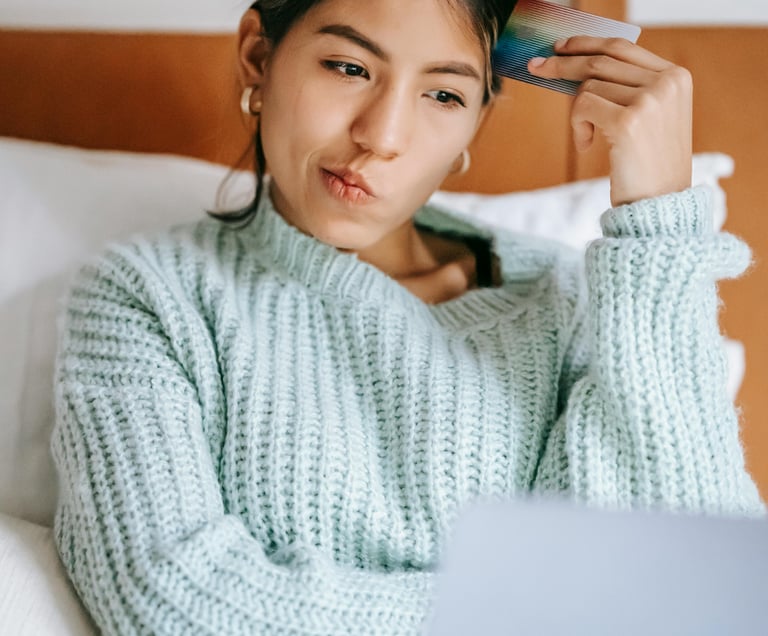 A thoughtful woman using a credit card and laptop for online shopping while sitting in bed.
