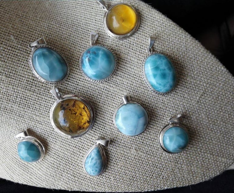 Dijes de piedras preciosas como Larimar y Ámbar sobre una superficie con textura color crema.