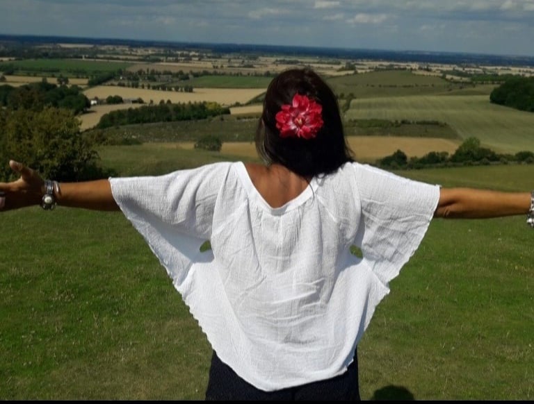 An image of the back of Sheila Cristina on the top of a hill. In front of her is a beautiful view of many fields in England.