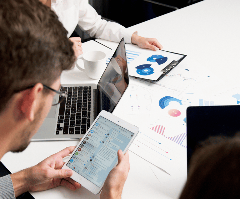 un hombre sentado a una mesa con una tablet y un portátil viendo analíticas de redes sociales