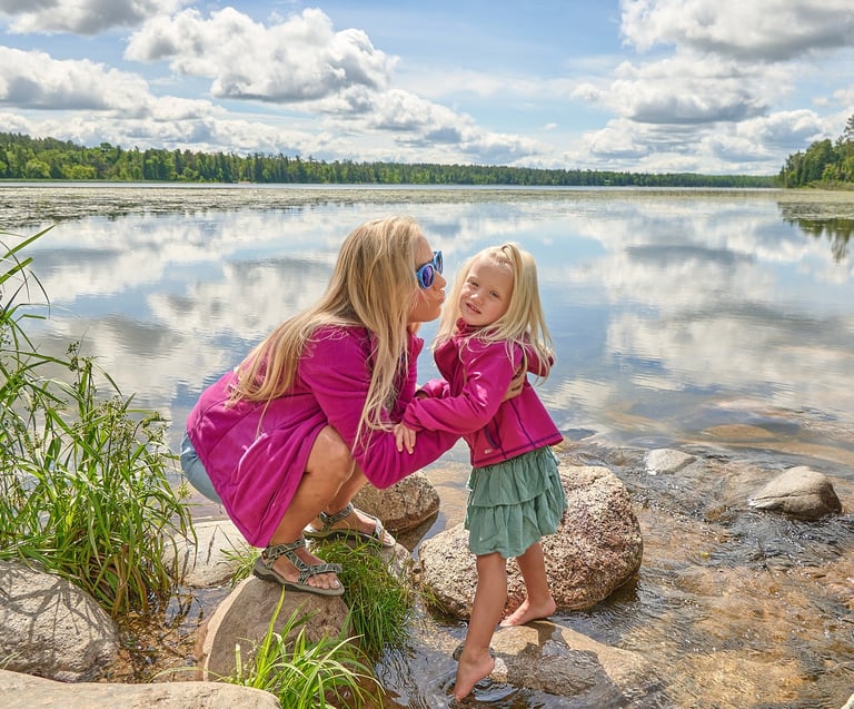 a mother and her girl in pink jackets standing in front of a lake