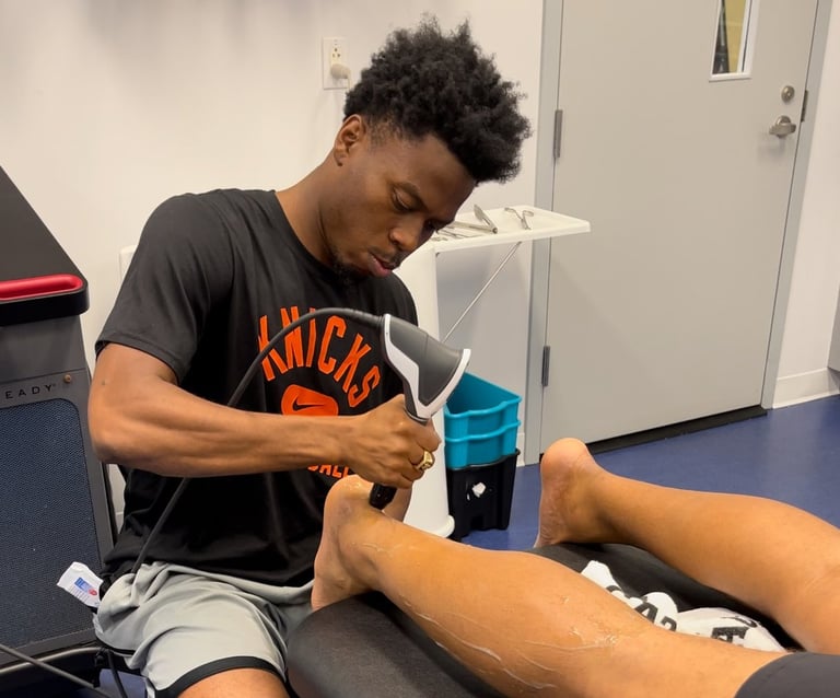 Sports medicine therapist performing leg recovery therapy using shockwave treatment on athlete