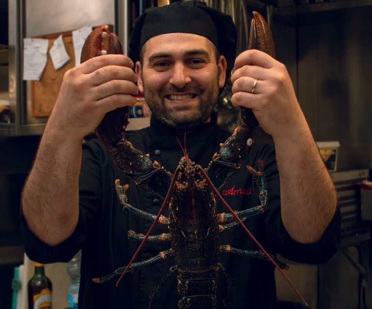 Chef Vito Amodio in cucina con divisa, sorridente mentre tiene in mano un grande astice vivo