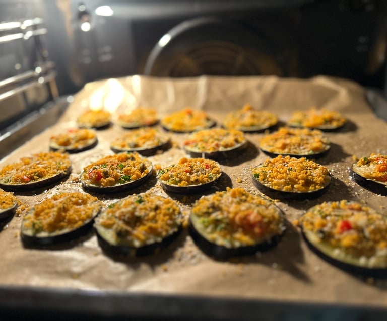 Slices of roasted eggplant with breadcrumb topping baking on a parchment-lined tray in an oven.