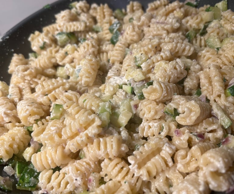 Creamy radiatori pasta salad with diced cucumbers and fresh herbs in a large bowl.