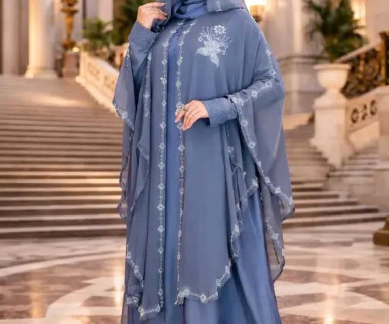 Elegant woman wearing a dusty blue modest abaya dress with floral embroidery and matching hijab.
