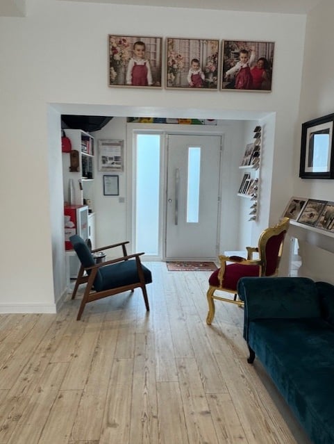 Modern home entryway with wood flooring, velvet chairs, and framed family portraits on a white wall.